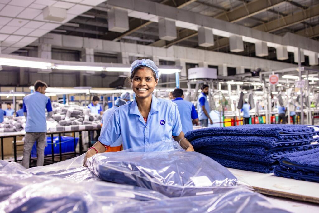 Smiling female textile worker organizing blue fabric in a bustling factory.