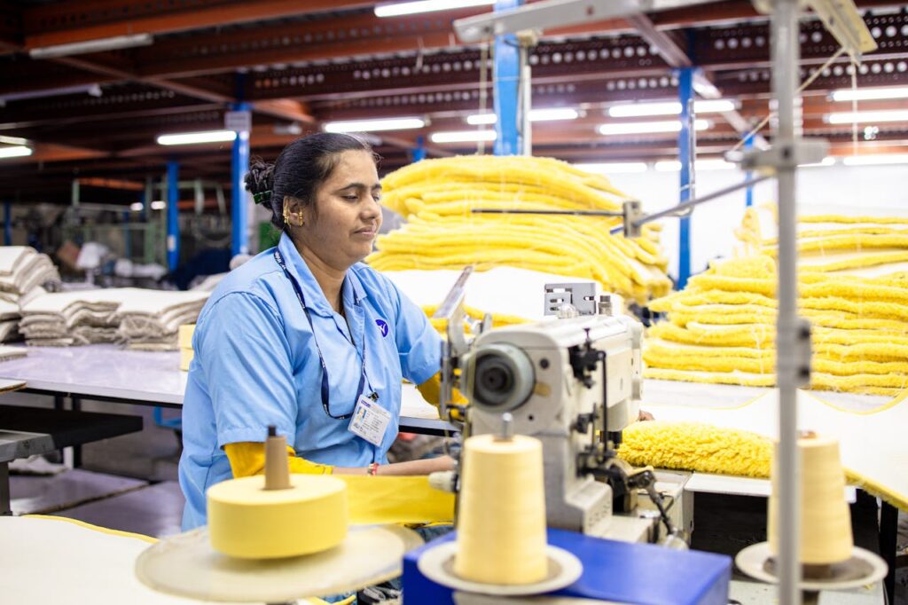 Female textile worker in a factory operating a sewing machine amidst piles of fabric.
