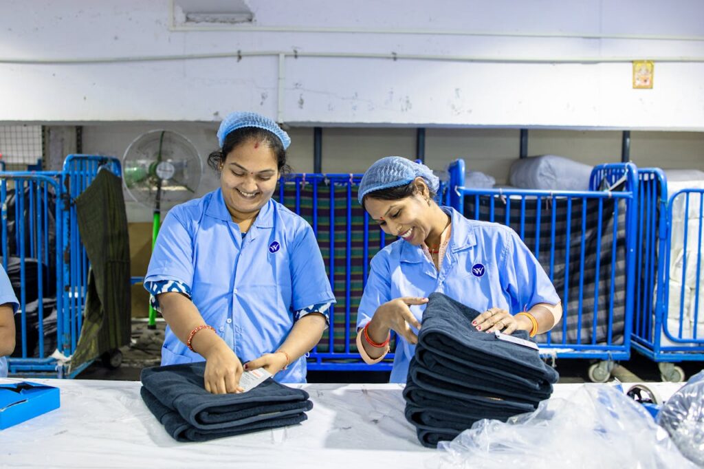 Two Indian female workers folding fabric in a textile factory, smiling and engaged in teamwork.