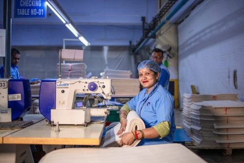Female textile worker operates a sewing machine in a bright factory setting.