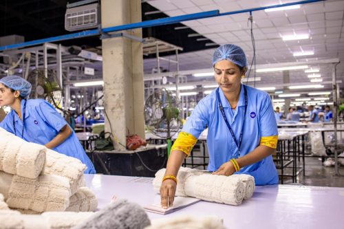 Indian textile worker organizing fabric rolls in a factory setting.
