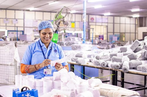 Indian female factory worker arranging towels in textile mill, showcasing productivity and joy.