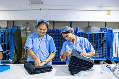 Two Indian female workers folding fabric in a textile factory, smiling and engaged in teamwork.