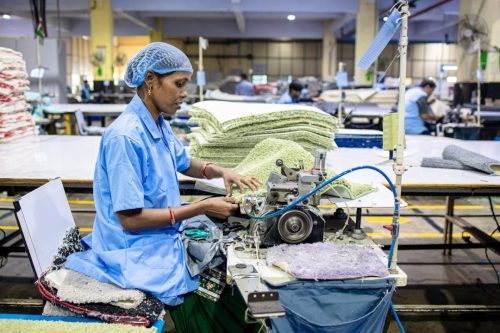 A female factory worker operates an industrial sewing machine in a textile factory, showcasing precision and skill.